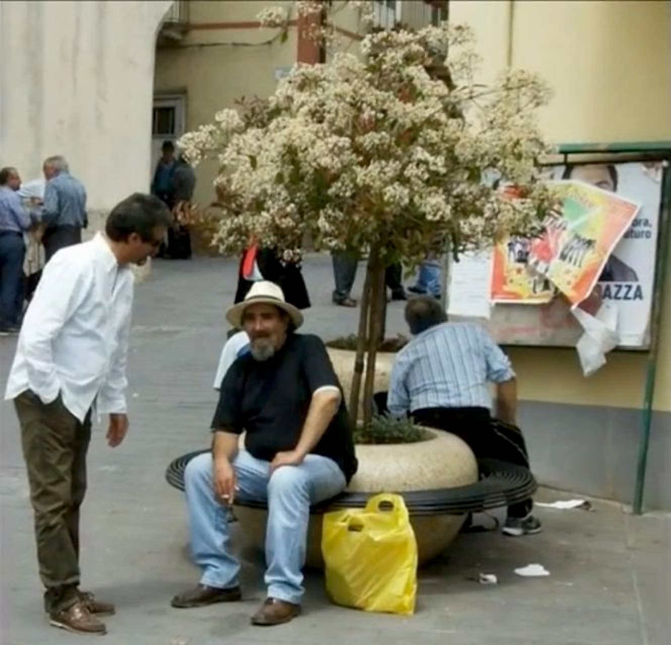 Enzo Schillizzi seduto in piazza con il cappello chiaro, tra la gente