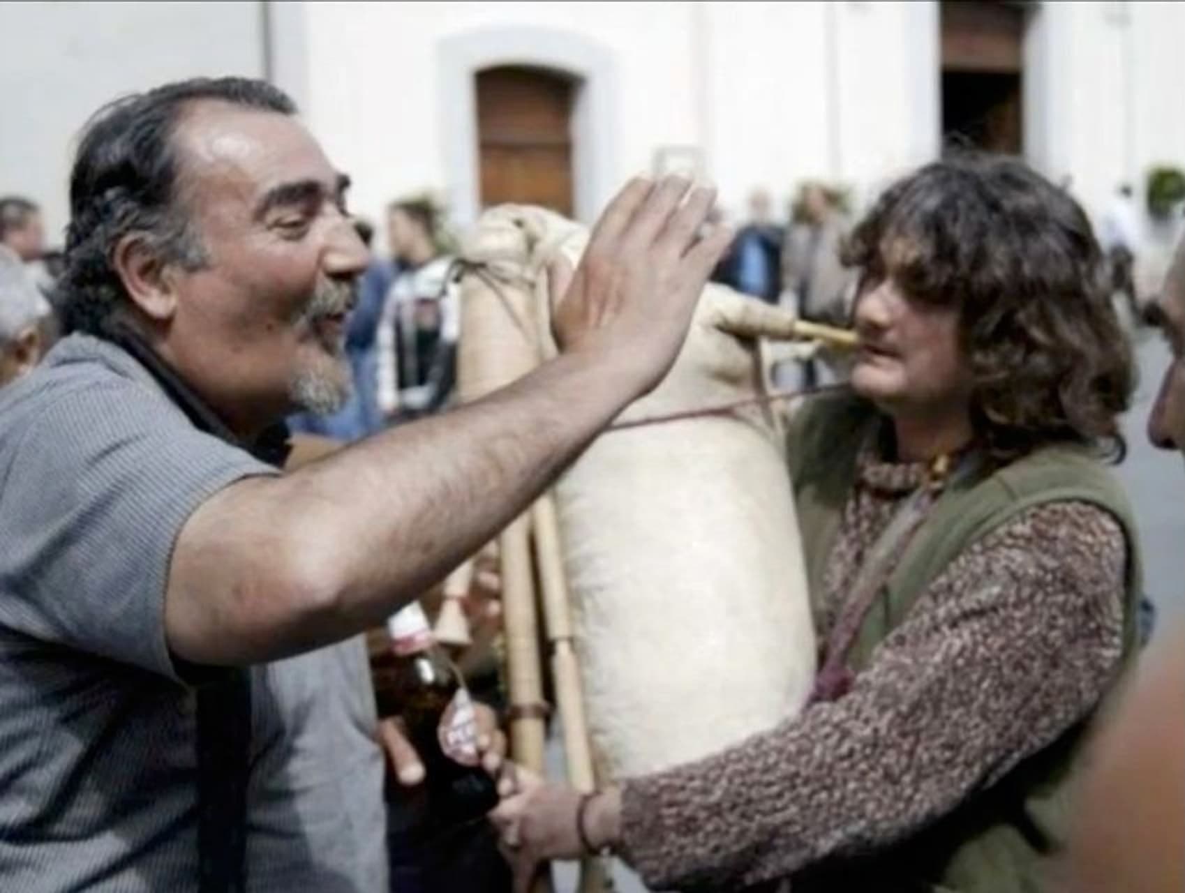Enzo Schillizzi alza la mano accanto a un suonatore di zampogna, durante una festa