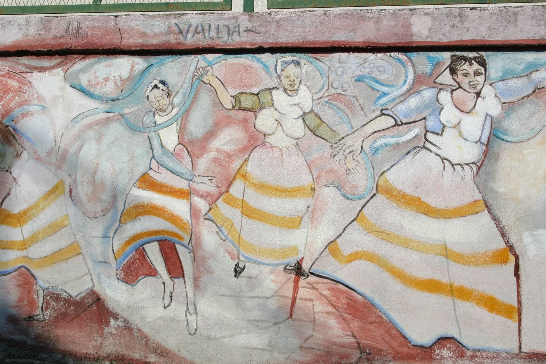 Donne in costume danzano lungo un muro, con le gonne a righe e i nastri nell’aria.