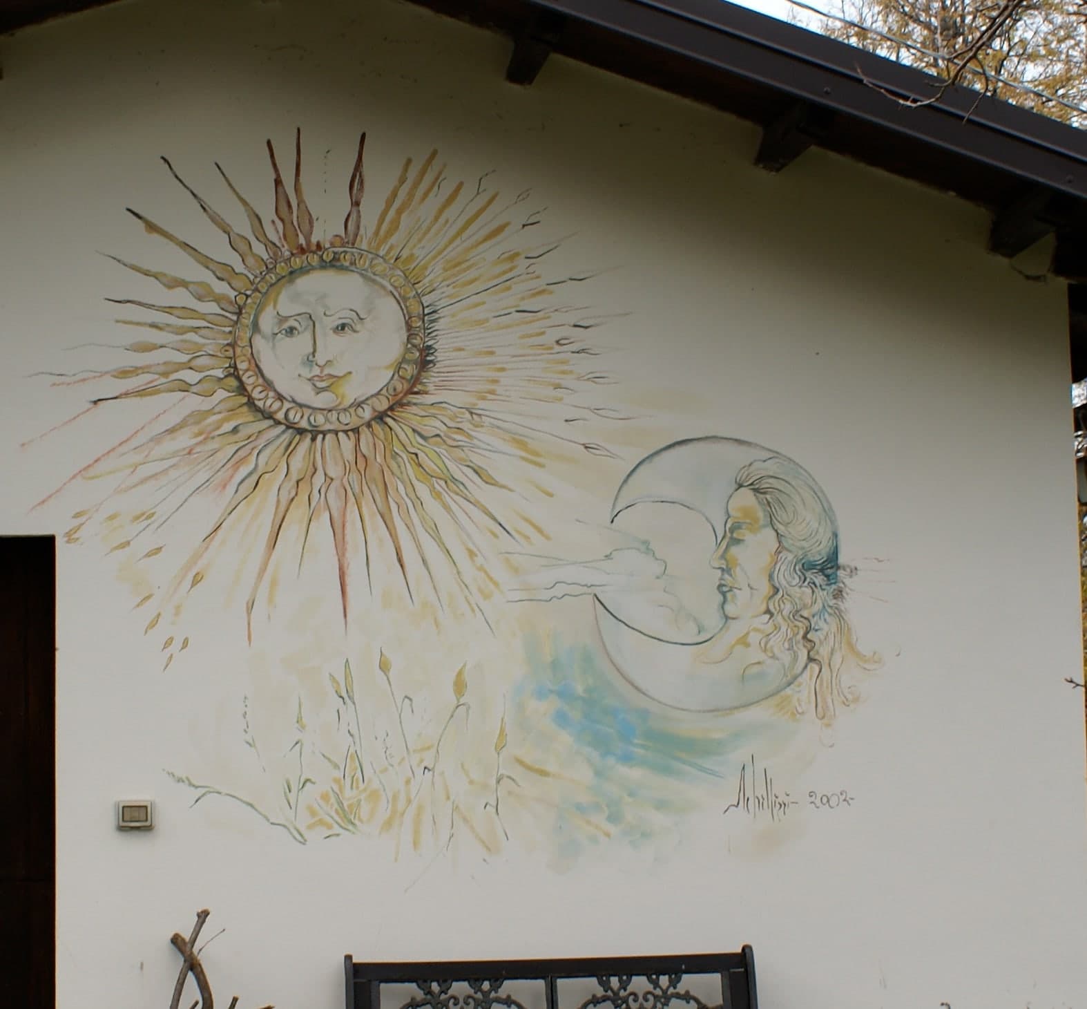 Il sole e la luna, con i loro volti, sotto il tetto di una casa. Firmato «Schillizzi 2002». A Francavilla sul Sinni.
