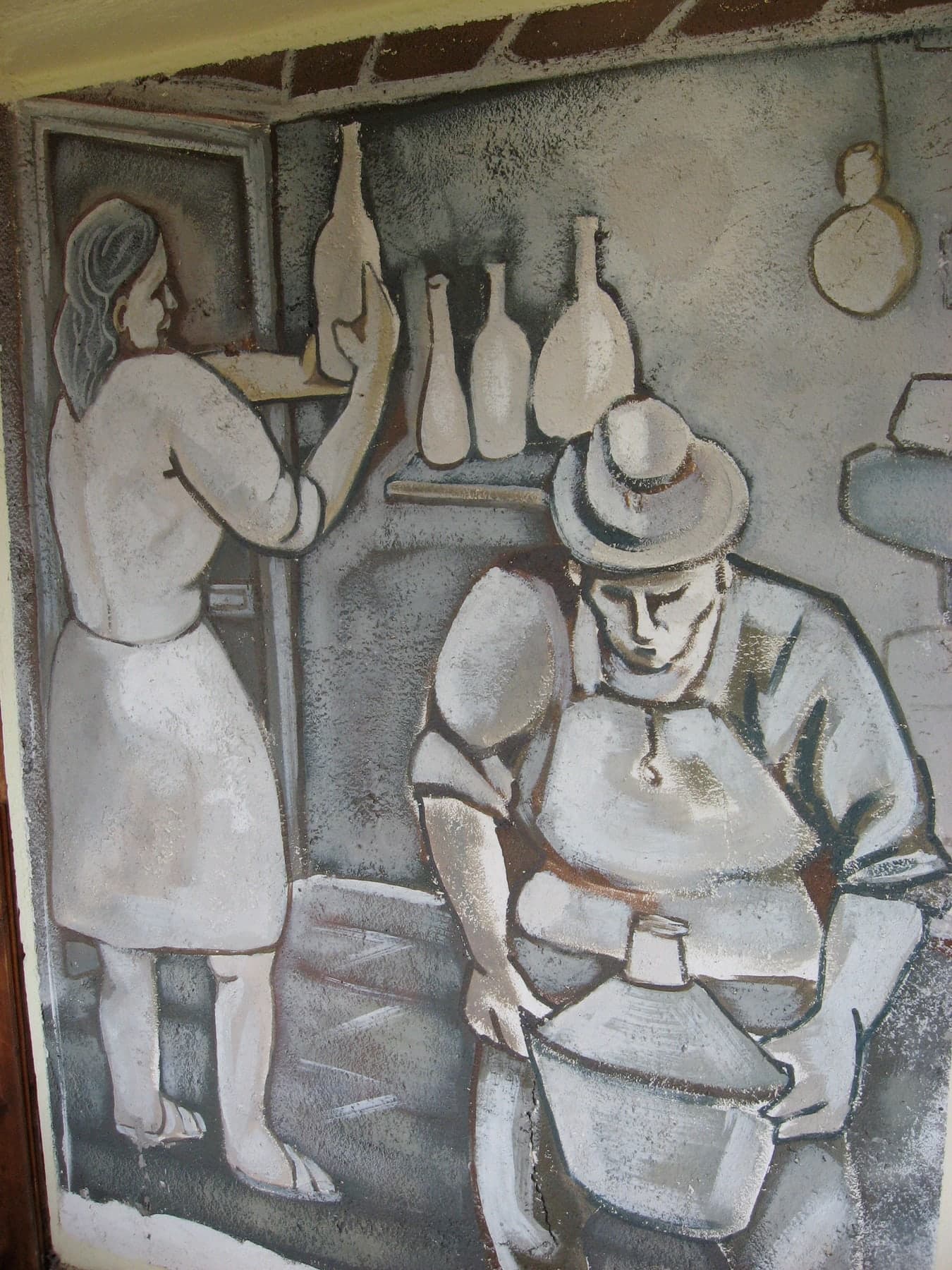 Una donna sistema le bottiglie sulla mensola; davanti, un uomo con il cappello chino sul lavoro. Al ristorante Luna Rossa di Terranova di Pollino.