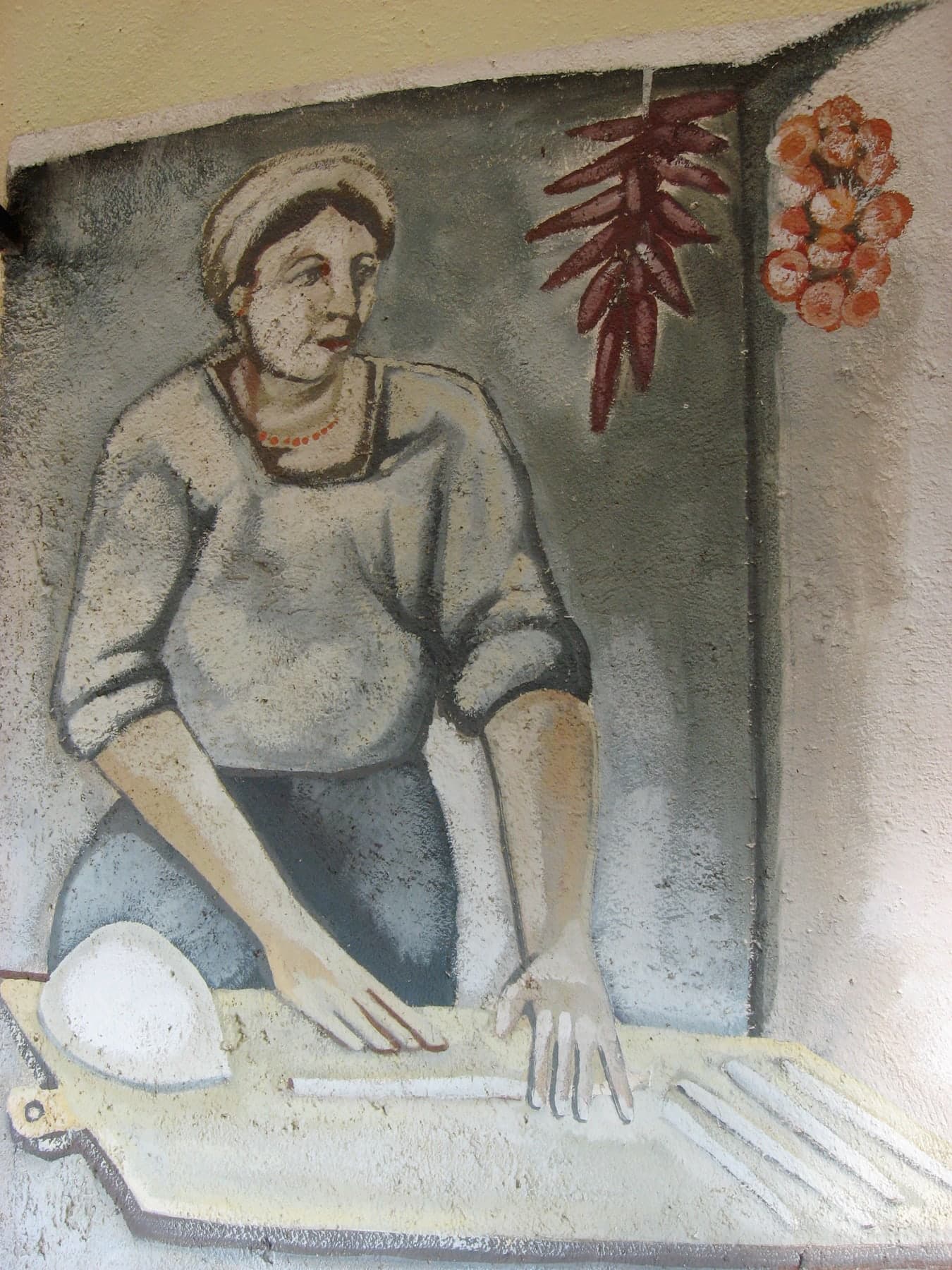 Una donna impasta sulla spianatoia; alle sue spalle, i peperoncini e le cipolle appesi. Al ristorante Luna Rossa di Terranova di Pollino.